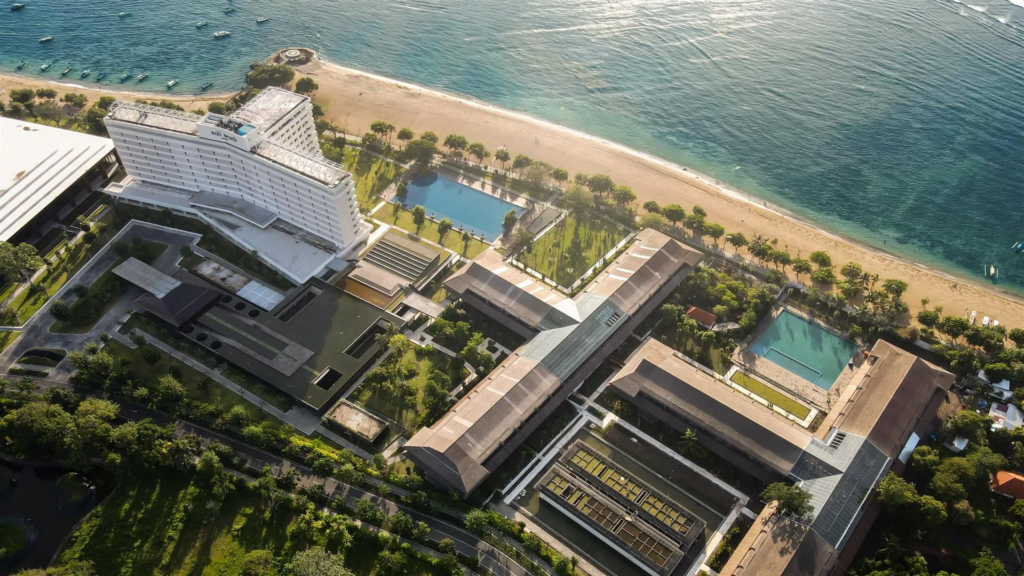 Oceanfront resort with infinity pool and tropical gardens under clear blue skies, showcasing the best time to visit Sanur for a relaxing beachfront stay.