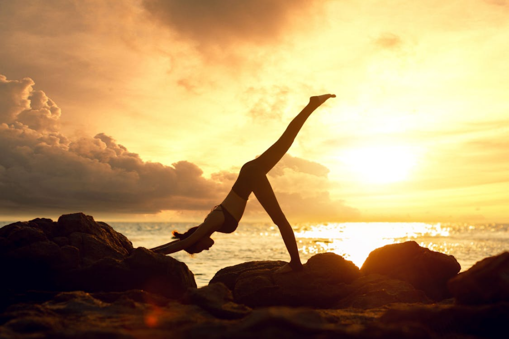 Woman practicing yoga in Bali at sunrise on a tropical beach, with calm ocean waves and palm trees in the background.