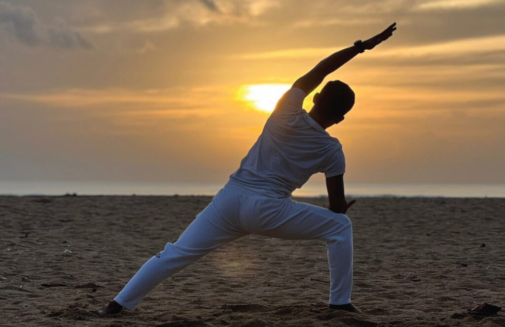 Woman practicing yoga in Bali at sunrise on a tropical beach, with calm ocean waves and palm trees in the background.