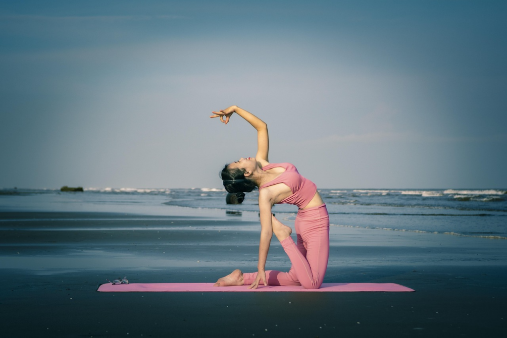 Woman practicing yoga in Bali at sunrise on a tropical beach, with calm ocean waves and palm trees in the background.